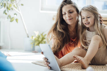 Smiling girl using tablet PC with mother at home - JOSEF23751