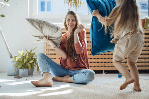 Cheerful mother and daughter playing pillow fight at home - JOSEF23752