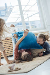Cheerful family playing with pillows on mat at home - JOSEF23755