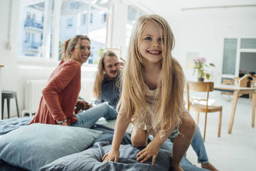 Lächelndes blondes Mädchen mit Mutter und Vater im Hintergrund - JOSEF23762