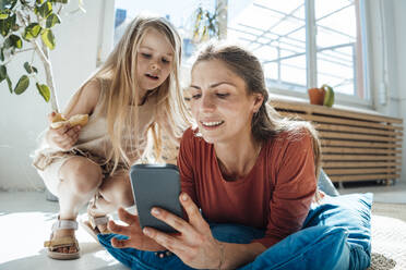 Lächelnde Frau mit Smartphone und Tochter mit Snack zu Hause - JOSEF23772