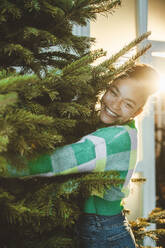 Smiling woman embracing Christmas tree - JOSEF23786