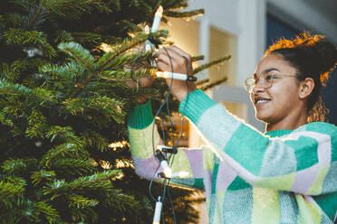 Young woman decorating Christmas tree with fairy lights - JOSEF23791