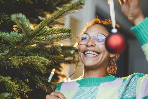 Happy woman decorating Christmas tree with bauble - JOSEF23793