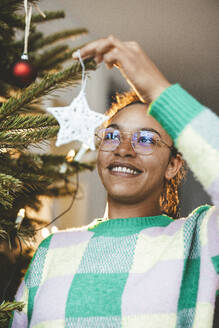 Smiling woman hanging star on Christmas tree - JOSEF23794