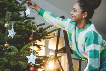 Junge Frau hängt Stern an Weihnachtsbaum - JOSEF23801