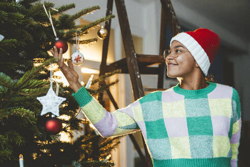 Junge Frau betrachtet eine Christbaumkugel am Weihnachtsbaum - JOSEF23803