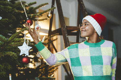 Young woman looking at bauble on Christmas tree - JOSEF23803