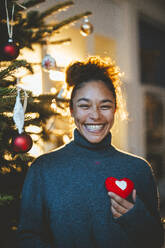 Happy woman with red heart shape at home - JOSEF23826