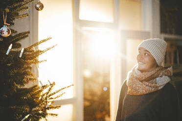 Frau in warmer Kleidung betrachtet den Weihnachtsbaum - JOSEF23828