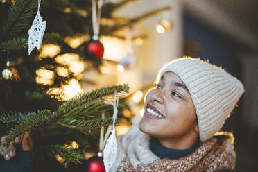 Lächelnde Frau mit Strickmütze betrachtet den Weihnachtsbaum - JOSEF23831