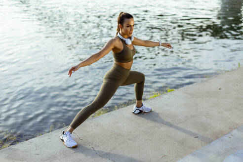 Pretty young woman in sportswear stretching on a river promenade - INGF12987