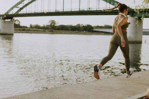 View at active young beautiful woman running on the promenade along the riverside - INGF12988