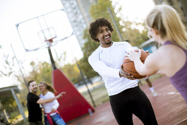 Multiracial couple playing basketball on outdoor court at outumn day - INGF13002