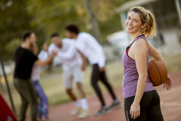 Portrait of fitness young woman with basketball ball playing game outdoor with friends - INGF13004