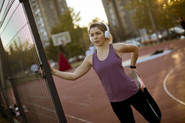 Pretty young woman with earphones stretching during sport training - INGF13009