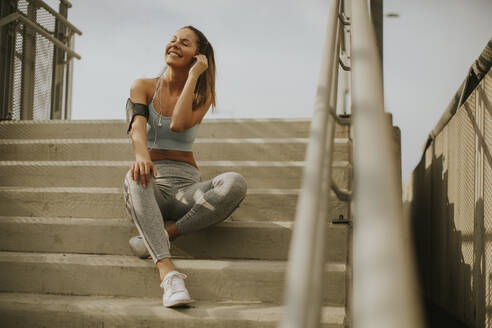 Portrait of pretty young female runner resting on the stairs - INGF13018