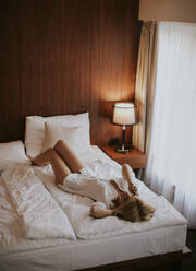 Happy womanl using a mobile phone lying on the bed at home - INGF13026