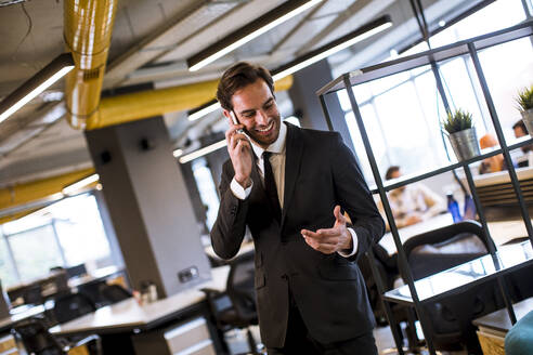 Handsome young businessman wearing black suit using modern smartphone in the office - INGF13065