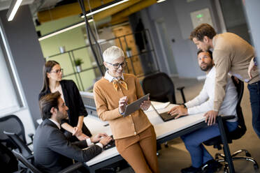 Group of business people working and communicating while standing in the office together with colleagues sitting in the background - INGF13077