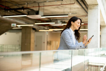 Pretty young business woman using mobile phone in the office hallway - INGF13089