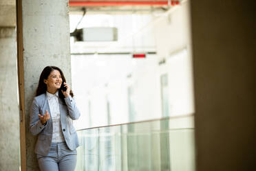 Pretty young business woman using mobile phone in the office hallway - INGF13090