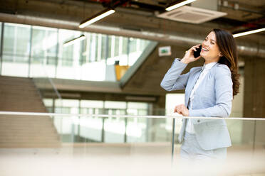 Pretty young business woman using mobile phone in the office hallway - INGF13091