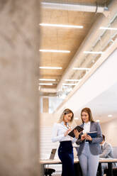 Two pretty young business women looking at financial results on digital tablet in front of their team at the office - INGF13092