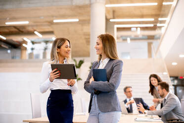 Two pretty young business women looking at financial results on digital tablet in front of their team at the office - INGF13093