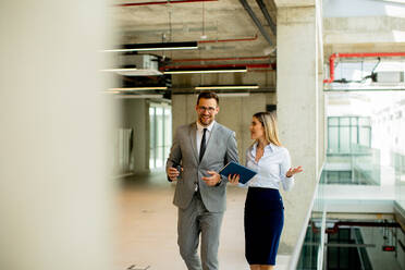 Young coworkers walking and talking along corridor in the modern office - INGF13097