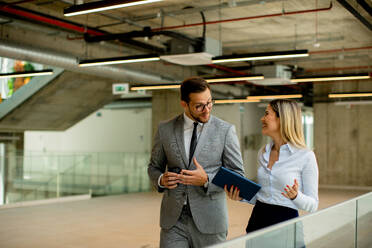 Young coworkers walking and talking along corridor in the modern office - INGF13098