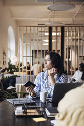 Female entrepreneur talking on smart phone while looking away at coworking office - MASF43001