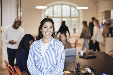 Portrait of smiling female entrepreneur wearing striped shirt at coworking office - MASF43003