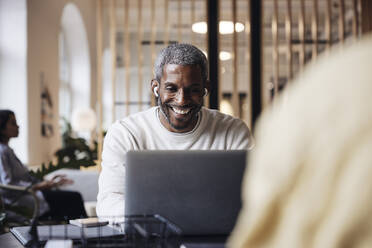 Happy businessman doing video call through laptop while sitting at office - MASF43008