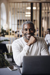 Portrait of smiling male business professional sitting with laptop at office - MASF43009