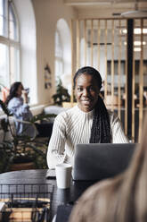 Portrait of smiling businesswoman sitting at desk in coworking office - MASF43017