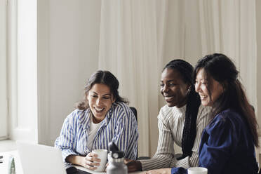 Happy female business professionals watching laptop while sitting at desk in coworking office - MASF43031