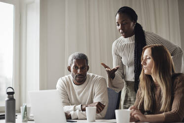 Businesswoman explaining colleagues while looking at laptop in office - MASF43034