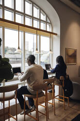 Male and female business colleagues working on laptop while sitting on chair at coworking office - MASF43041