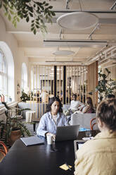 Businesswoman using laptop while working with colleagues at coworking office - MASF43044