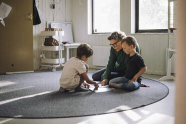 Preschool kids studying with senior female teacher while sitting on carpet in classroom at school - MASF43051