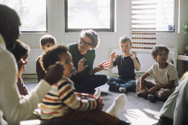 Senior female teacher playing with group of preschool children while sitting in classroom at kindergarten - MASF43055