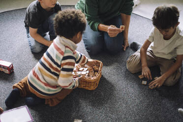 High angle view of schoolboys playing puzzle game with female teacher in classroom at kindergarten - MASF43056