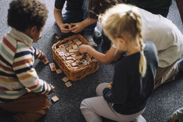 High angle view of preschool kids playing puzzle game while sitting in classroom at day care center - MASF43057