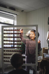 Smiling girl leaning to count while using abacus in classroom at preschool - MASF43059