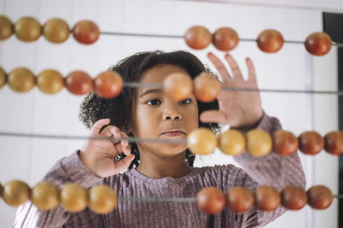 Girl with curly hair learning to count using abacus in classroom at kindergarten - MASF43062