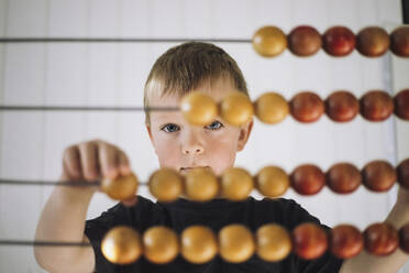 Portrait of schoolboy using abacus to count in classroom at kindergarten - MASF43064