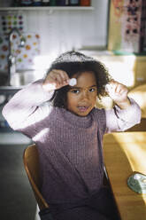 Portrait of girl showing clay art while sitting at bench in classroom at kindergarten - MASF43068