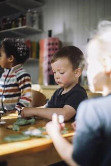 Schoolboy playing with clay while sitting at bench during art class at kindergarten - MASF43072