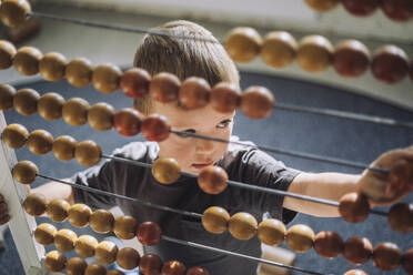 High angle view of boy leaning to count using abacus in classroom - MASF43073